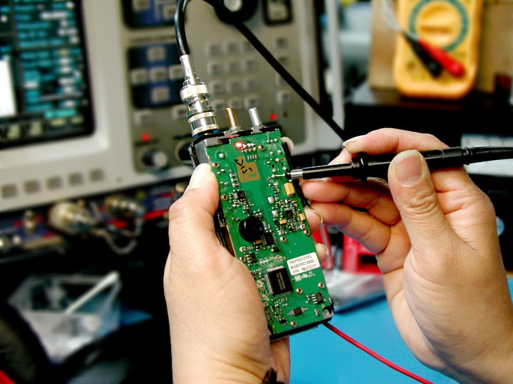 A 2-way radio repair specialist diagnoses the interior hardware of a handheld unit.