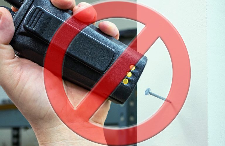 Two-Way Radio Mistakes: A red general prohibition sign is overlaid on a worker's hand as they use a two-way radio to hammer a nail into a wall.