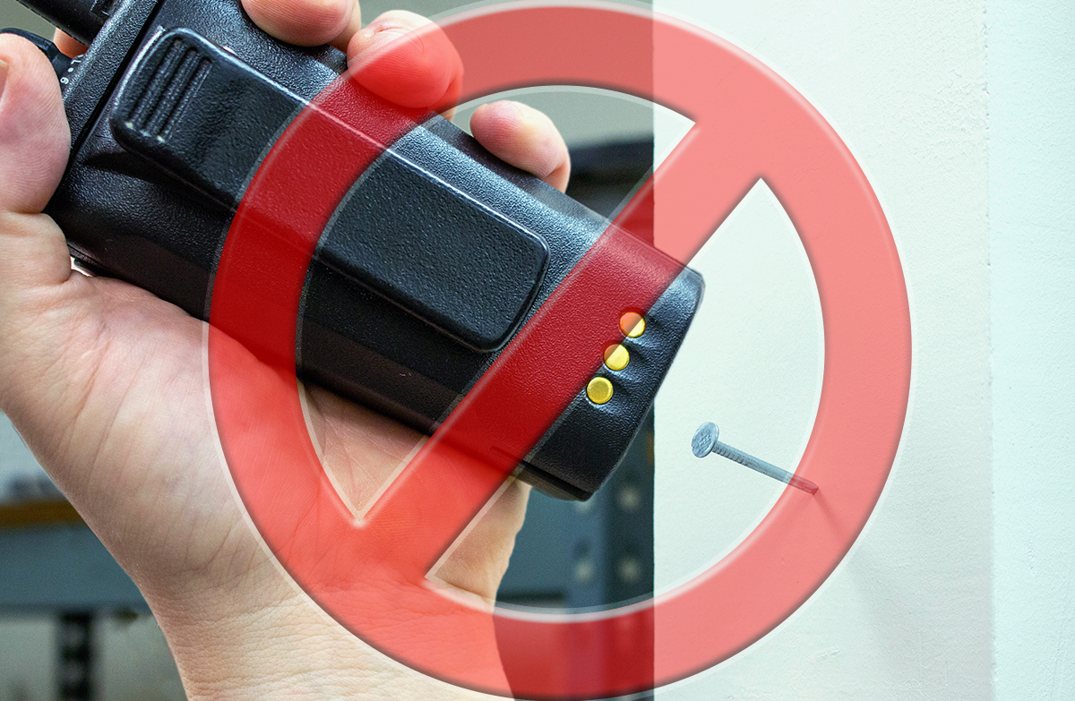 Two-Way Radio Mistakes: A red general prohibition sign is overlaid on a worker's hand as they use a two-way radio to hammer a nail into a wall.